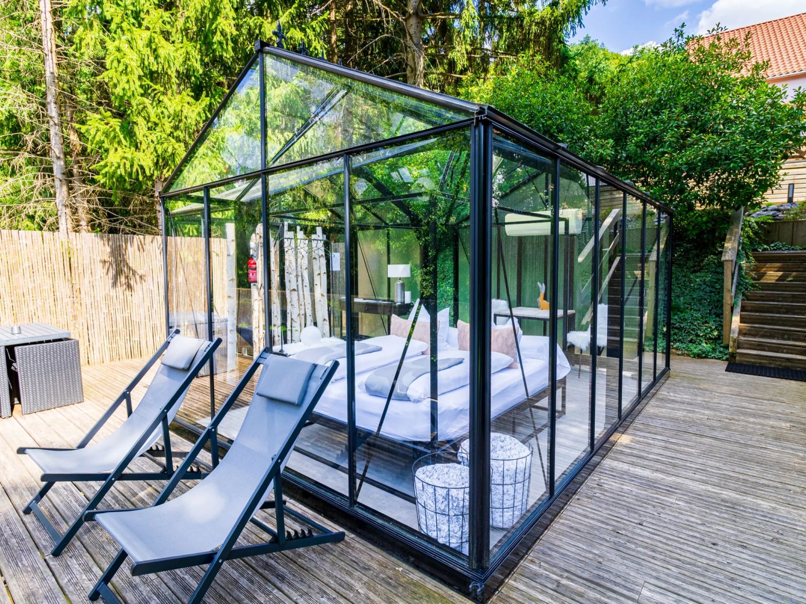 La Chambre de Verre, véranda vitrée à ossature noire sur terrasse en bois, avec lit double visible et chaises longues à La Grange d'Hélène